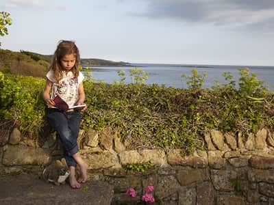 Child reading on a wall overlooking the sea at Marazion